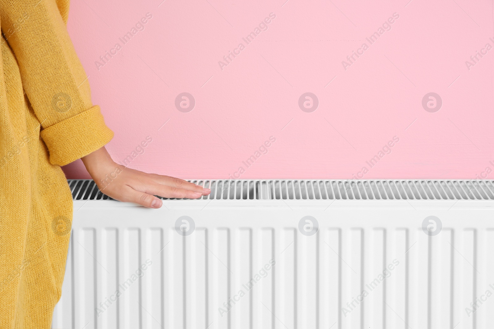 Photo of Woman warming hand on heating radiator near color wall