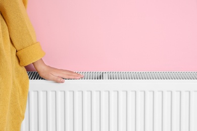 Photo of Woman warming hand on heating radiator near color wall