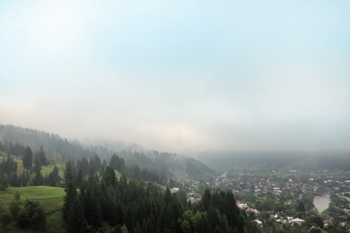 Photo of Picturesque landscape with small village and mountain forest covered in mist