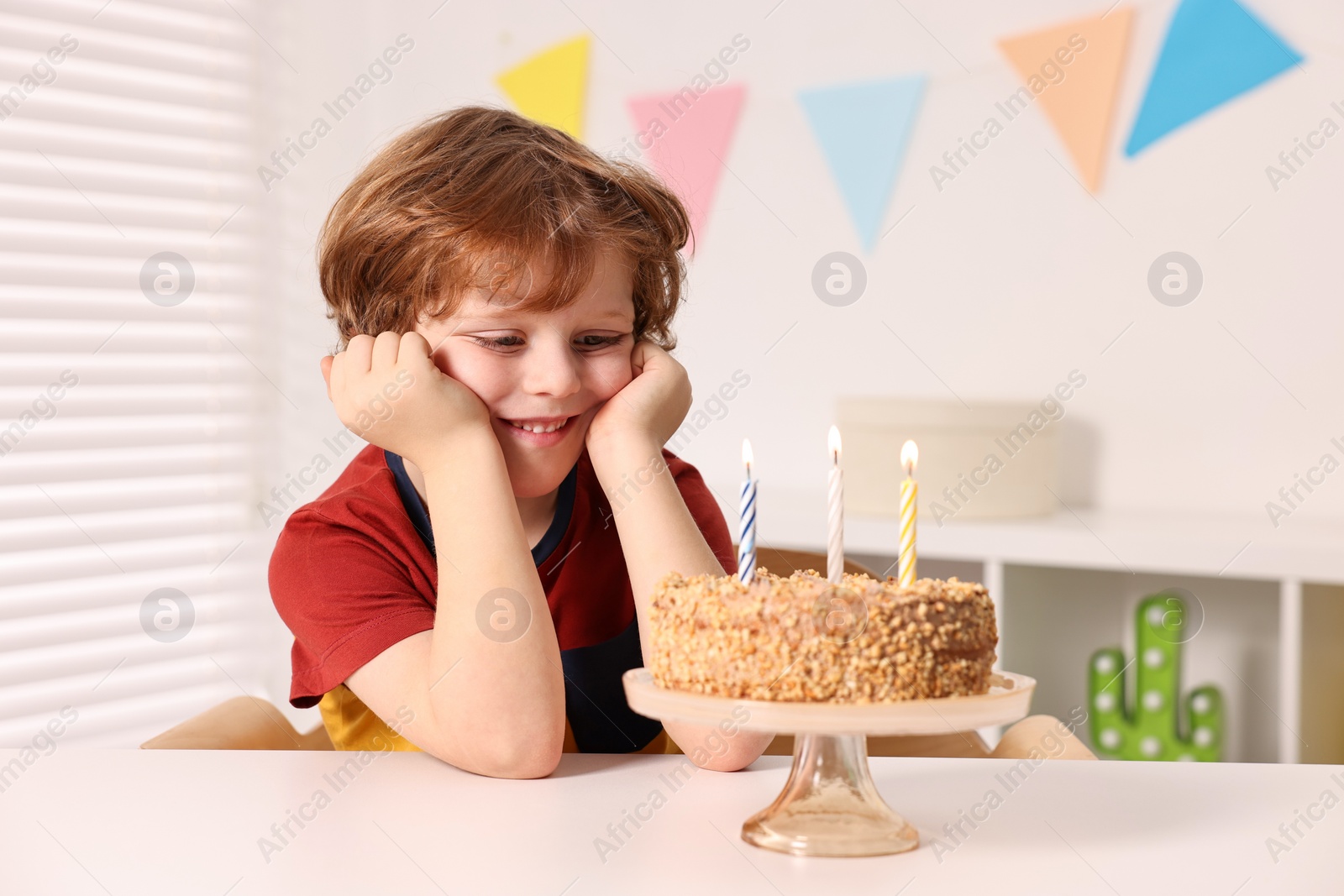 Photo of Cute boy with birthday cake at table indoors