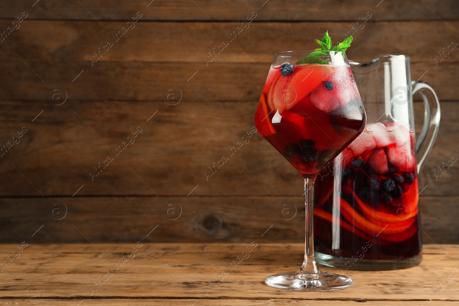 Photo of Glass and jug of Red Sangria with fruits on wooden table, space for text