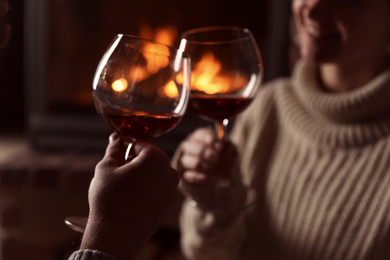 Photo of Lovely couple with glasses of wine near fireplace at home, closeup. Winter vacation