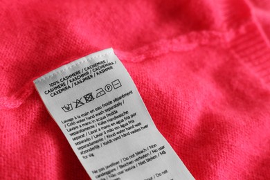 Clothing label in different languages on pink garment, closeup