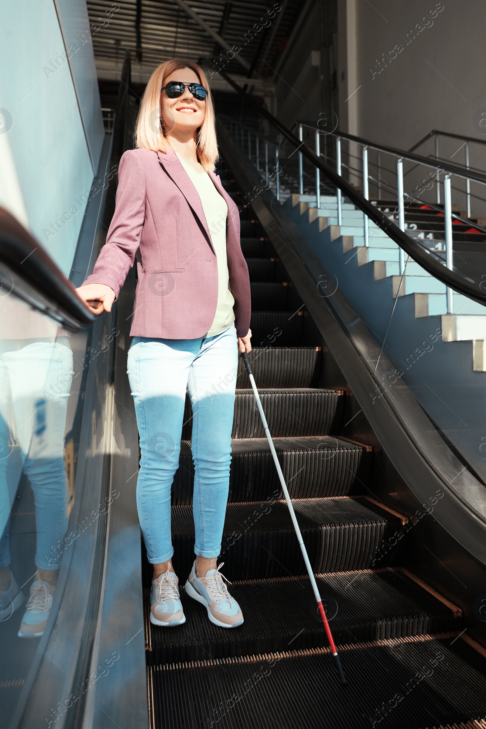 Photo of Blind person with long cane on escalator indoors