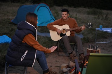 Photo of Couple with guitar sitting near bonfire at camping site
