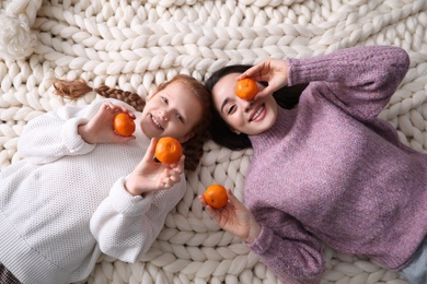 Photo of Happy girls with tangerines lying on knitted plaid, top view