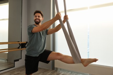 Man with hammock practicing fly yoga in studio