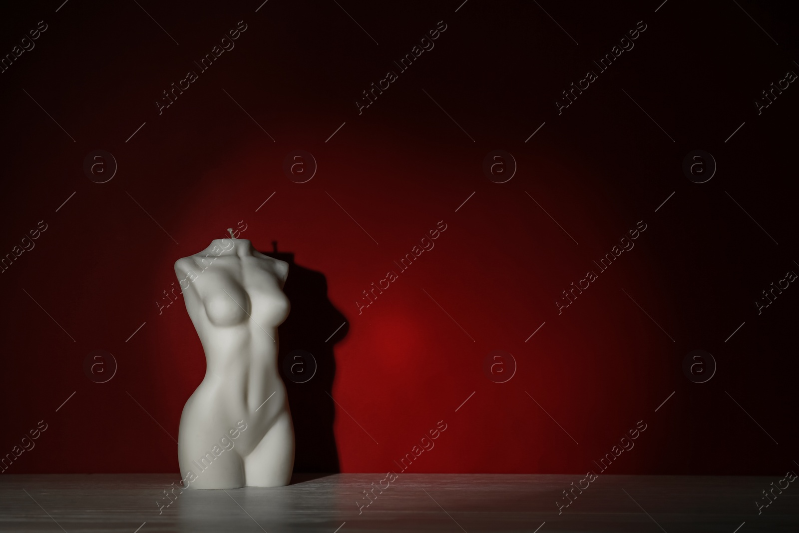 Photo of Beautiful female body shaped candle on white table near red wall, space for text