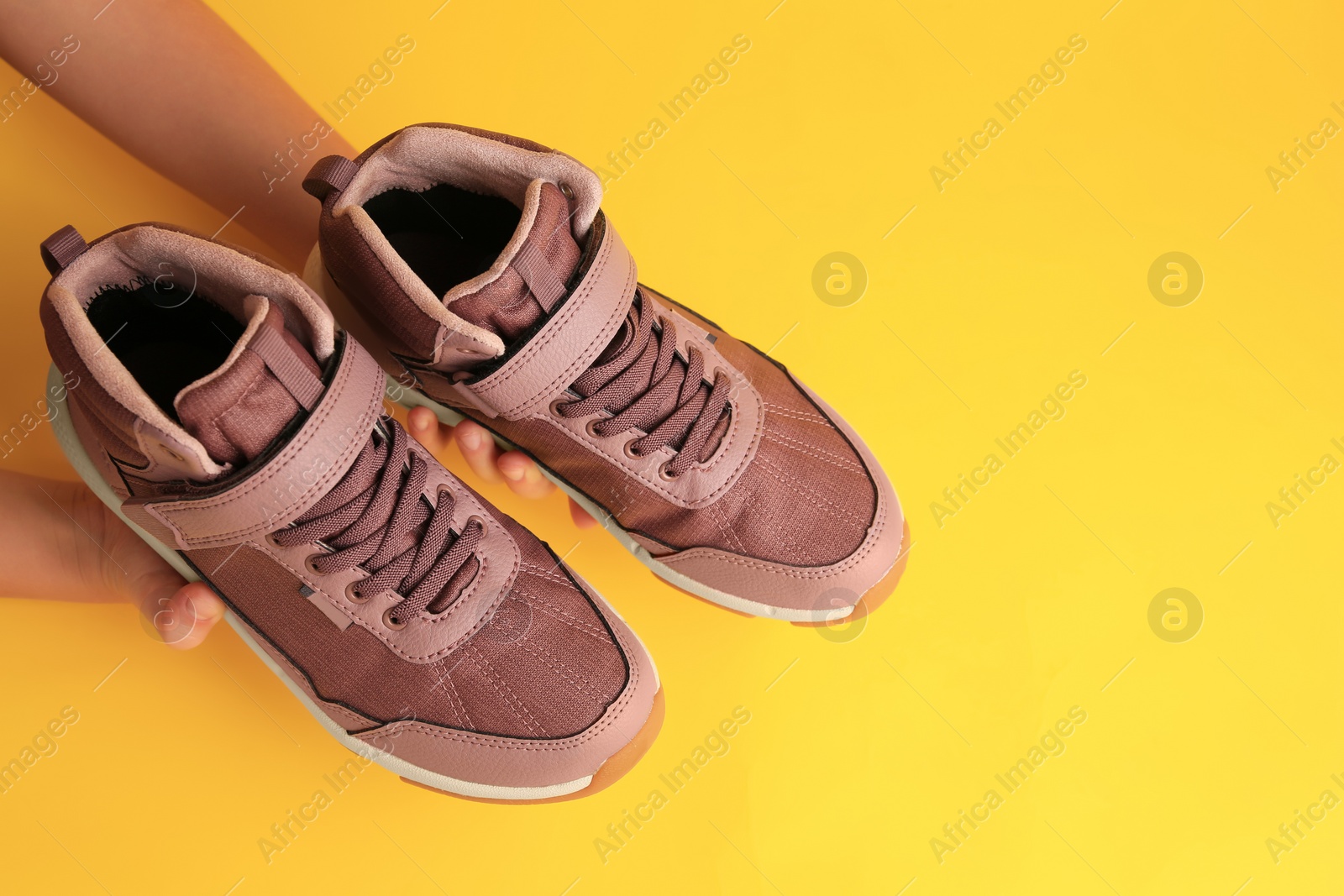 Photo of Girl holding stylish sneakers on yellow background, top view. Space for text