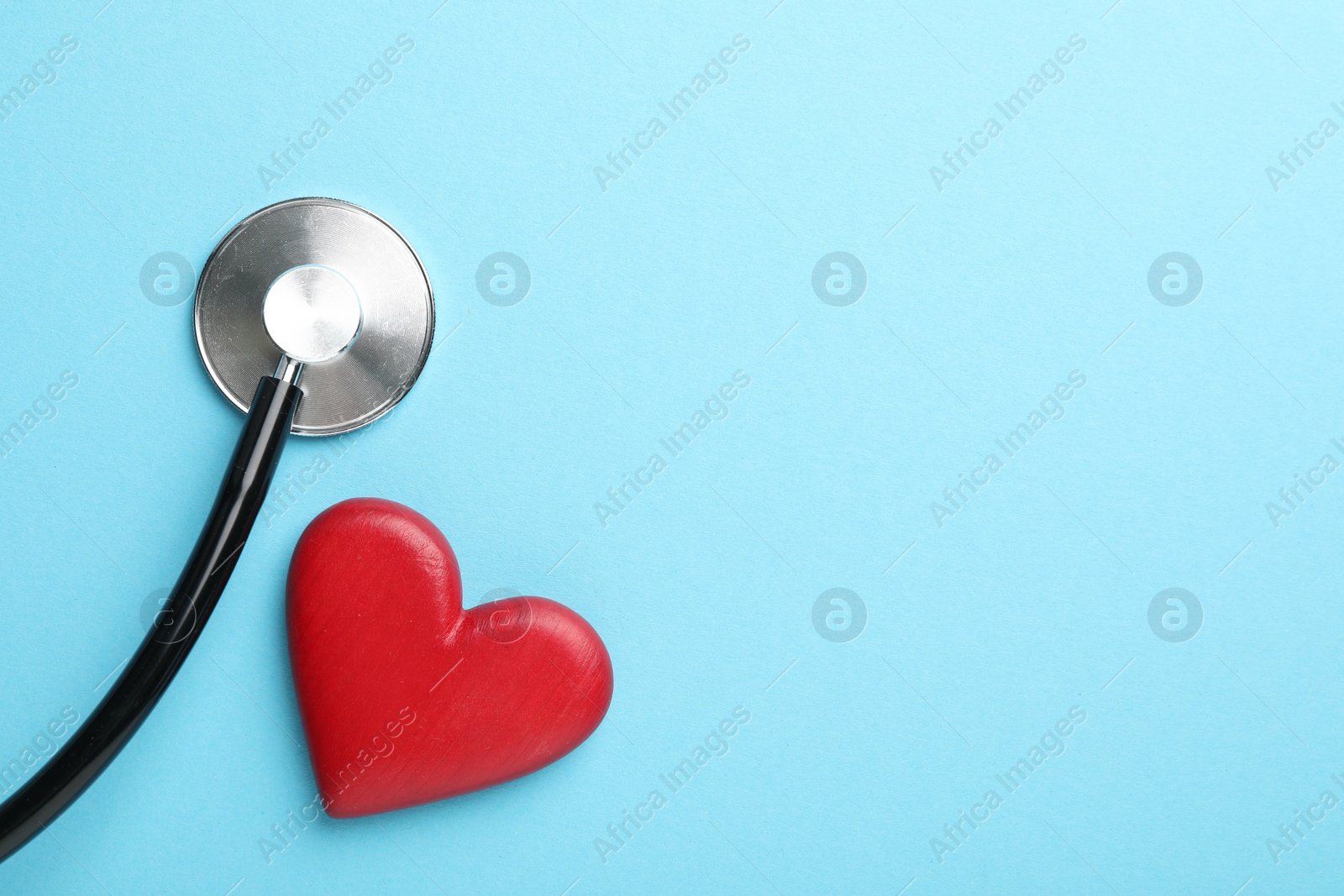 Photo of Stethoscope and red heart on light blue background, top view. Space for text