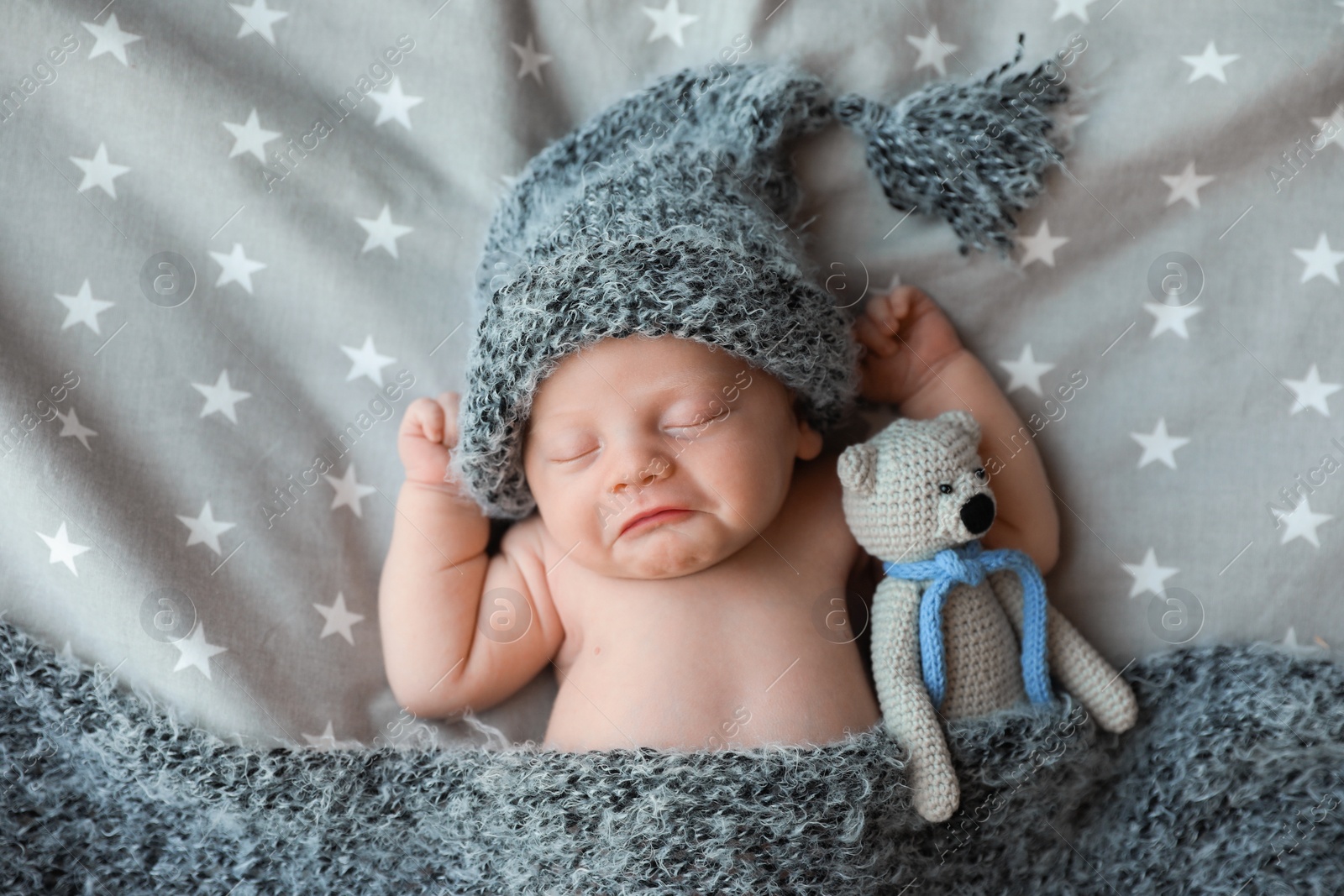 Photo of Cute newborn baby in warm hat with toy sleeping on bed, top view