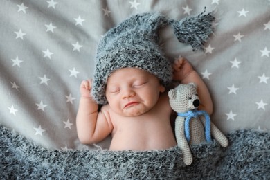 Photo of Cute newborn baby in warm hat with toy sleeping on bed, top view