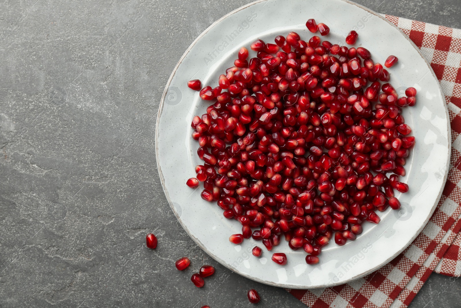 Photo of Tasty ripe pomegranate grains on grey table, top view. Space for text