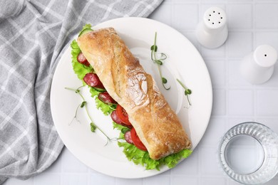 Delicious sandwich with sausages and vegetables served on white tiled table, flat lay