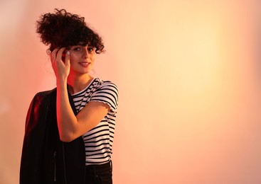 Beautiful young woman in black leather jacket posing on color background in neon lights. Space for text