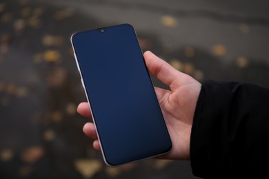 Woman holding phone outdoors on rainy day, closeup. Space or text