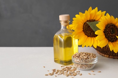 Photo of Sunflowers, bottle of oil and seeds on white table, space for text