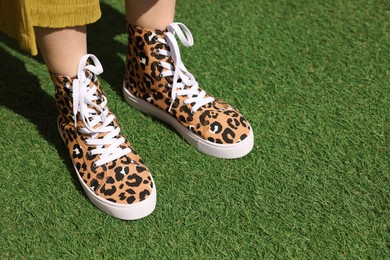 Photo of Woman wearing sneakers with leopard print on green grass outdoors, closeup. Space for text