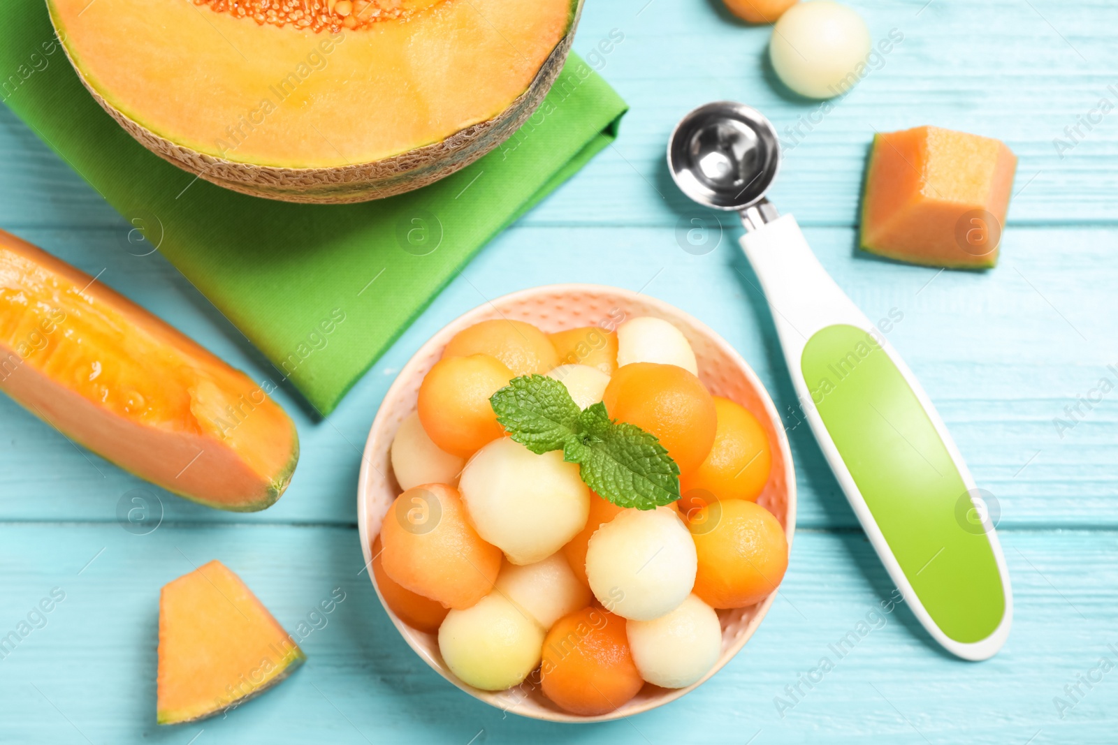Photo of Melon balls and mint in bowl on light blue table, flat lay