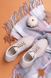 Photo of Fall fashion. Layout of woman's sneakers and scarf with fallen leaves on orange background, top view