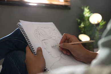 Photo of Man drawing portrait with pencil in notepad indoors, closeup
