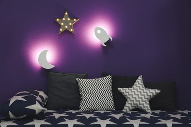 Photo of Room interior with bed and different night lamps on purple wall