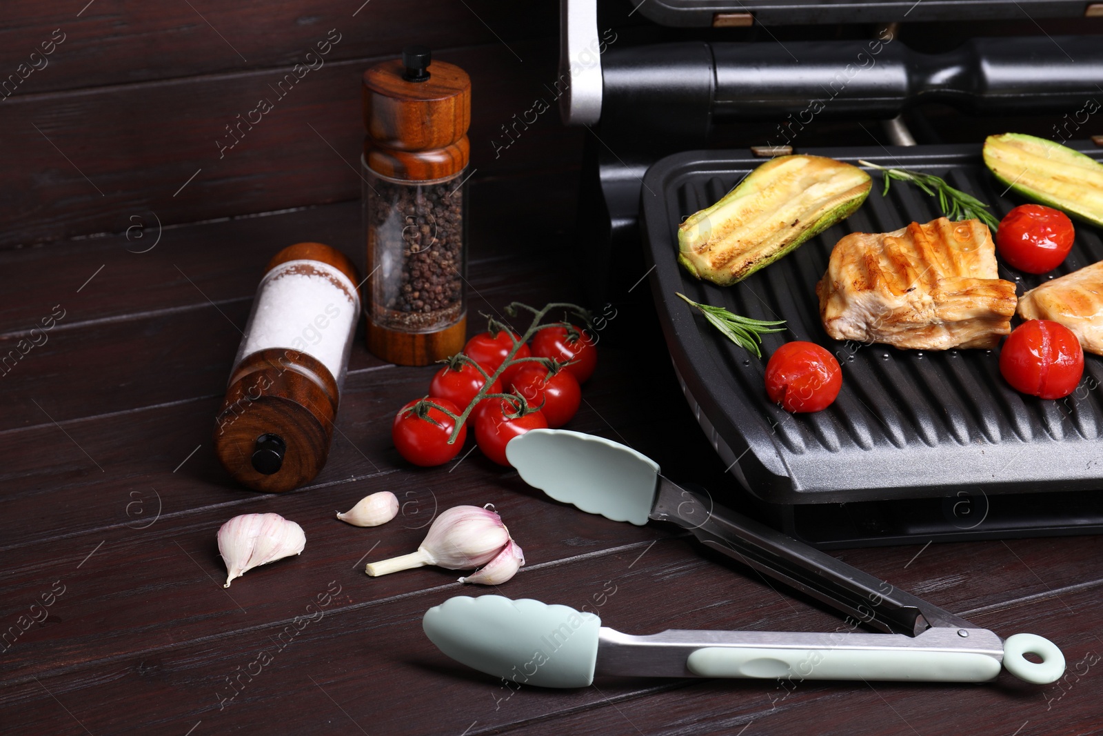 Photo of Electric grill with tasty meat, spices and vegetables on wooden table