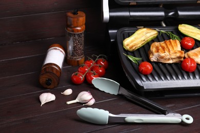 Photo of Electric grill with tasty meat, spices and vegetables on wooden table