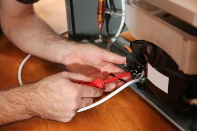 Photo of Male technician repairing broken refrigerator indoors, closeup