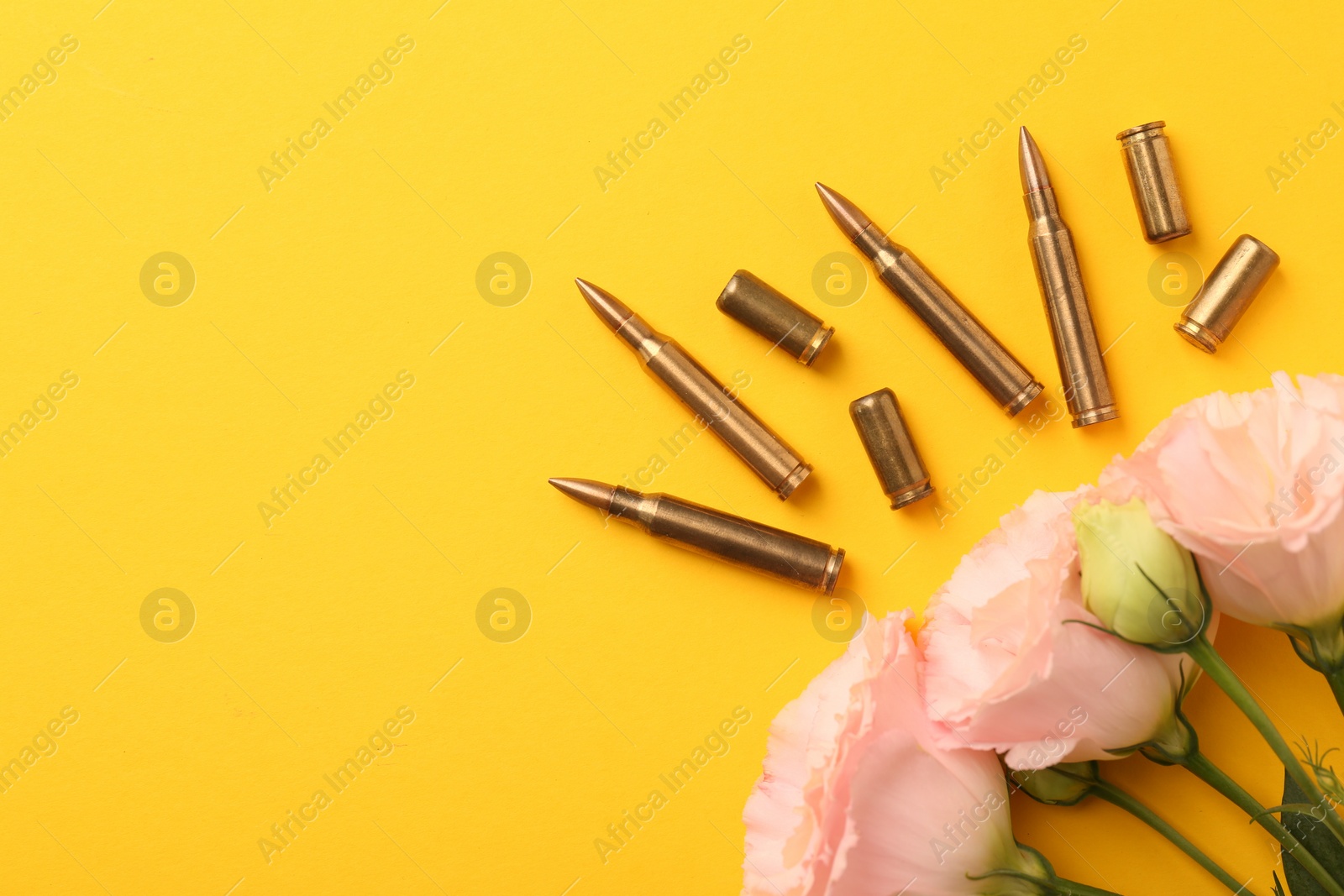 Photo of Bullets, cartridge cases and beautiful eustoma flowers on yellow background, flat lay. Space for text