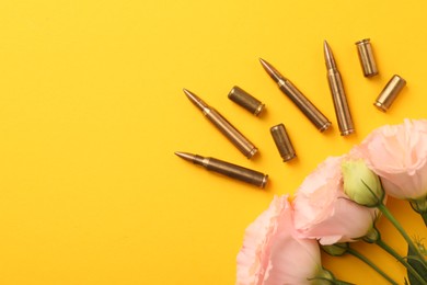 Bullets, cartridge cases and beautiful eustoma flowers on yellow background, flat lay. Space for text