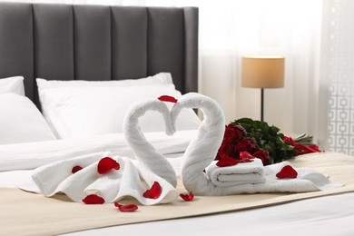 Photo of Honeymoon. Swans made of towels and beautiful red roses on bed in room