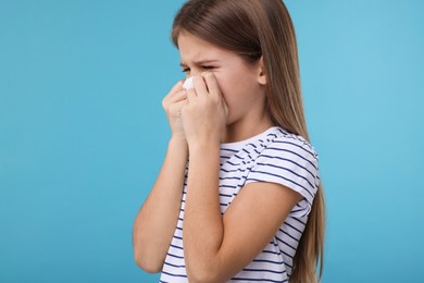 Sick girl with tissue coughing on light blue background, space for text