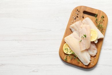 Photo of Pieces of raw cod fish, lemon and spices on white wooden table, top view. Space for text