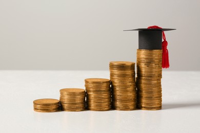 Scholarship concept. Graduation cap and stacked coins on white table