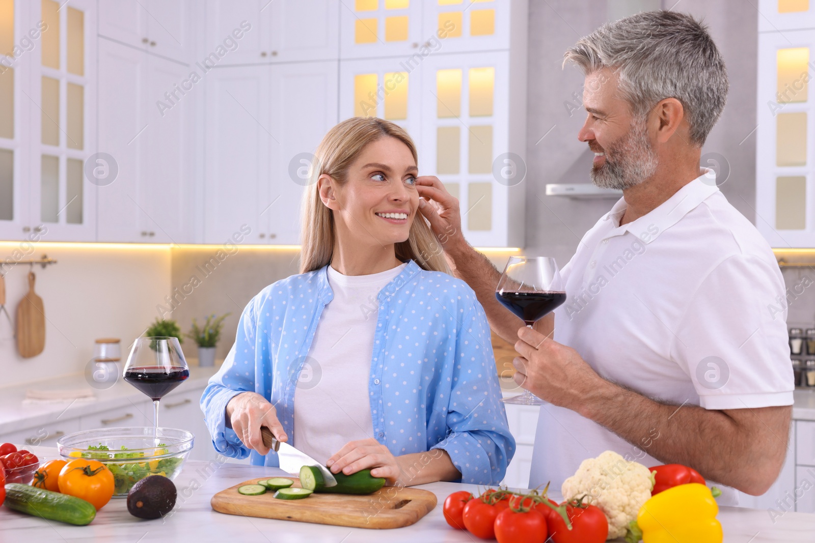 Photo of Happy affectionate couple cooking together at white table in kitchen