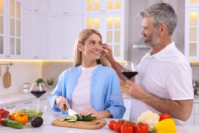 Photo of Happy affectionate couple cooking together at white table in kitchen