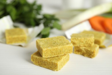 Photo of Bouillon cubes and other ingredients for soup on white wooden table, closeup