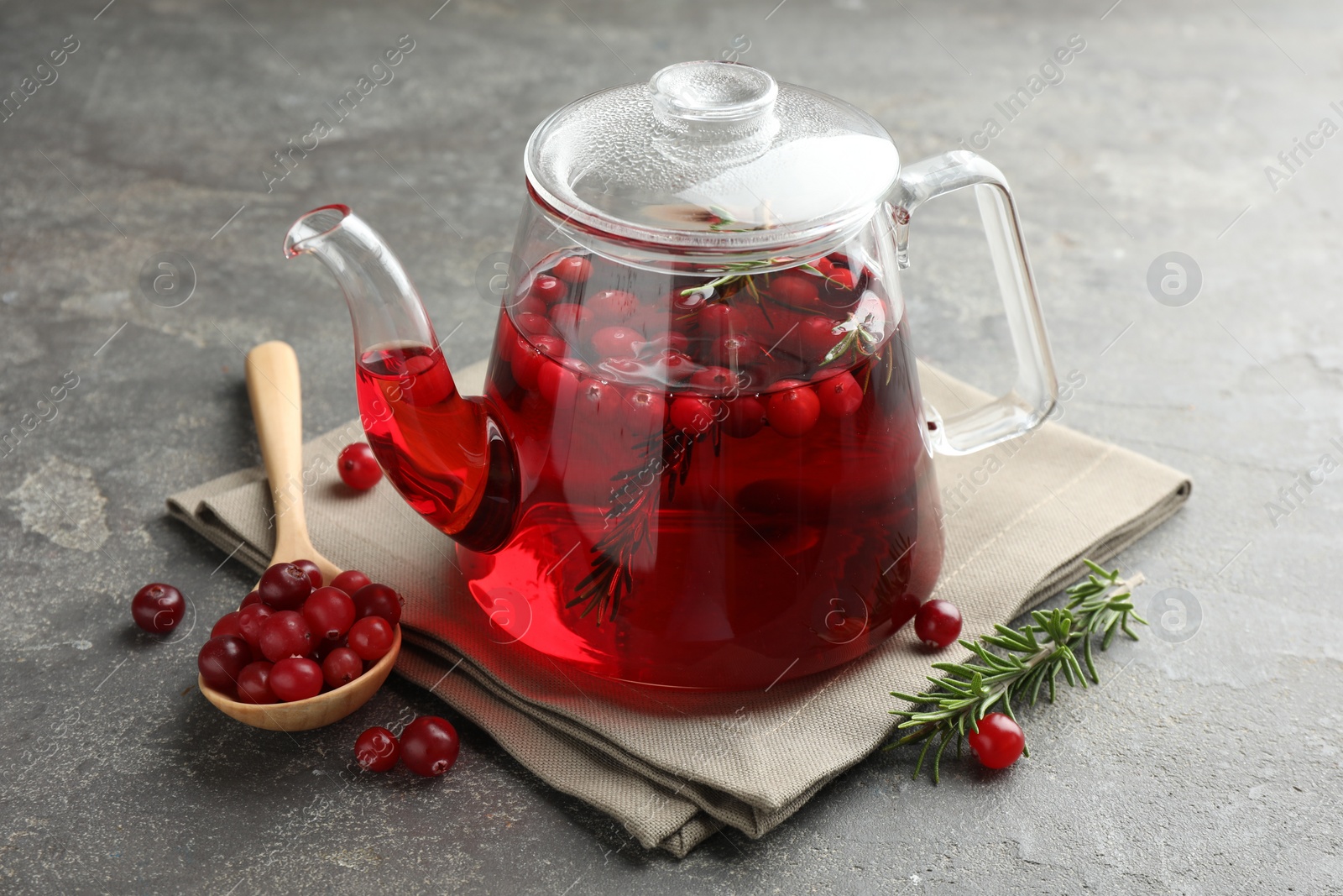 Photo of Tasty hot cranberry tea in teapot, rosemary and fresh berries on light grey textured table