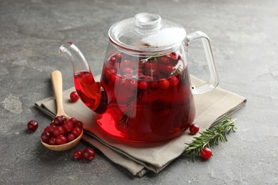 Photo of Tasty hot cranberry tea in teapot, rosemary and fresh berries on light grey textured table