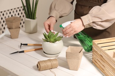 Woman spraying beautiful succulent plant with water at white wooden table, closeup