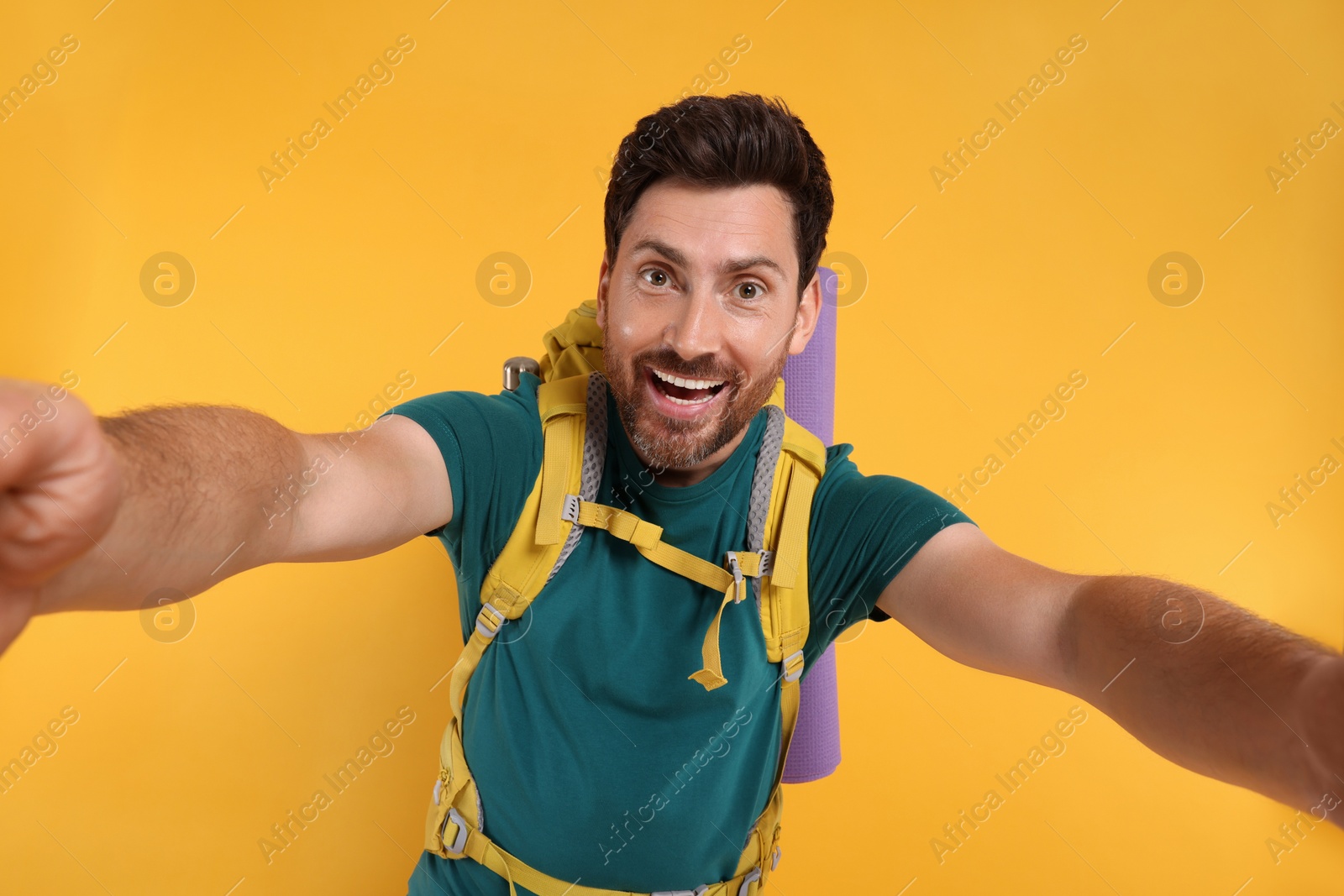 Photo of Happy man with backpack taking selfie on orange background. Active tourism