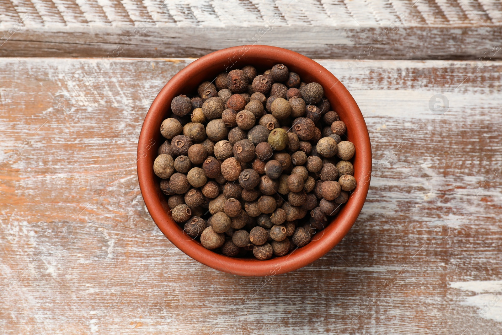 Photo of Aromatic allspice pepper grains in bowl on wooden table, top view