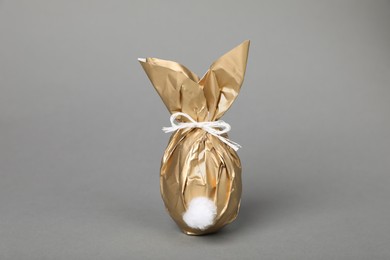 Photo of Easter bunny made of shiny gold paper and egg on grey background