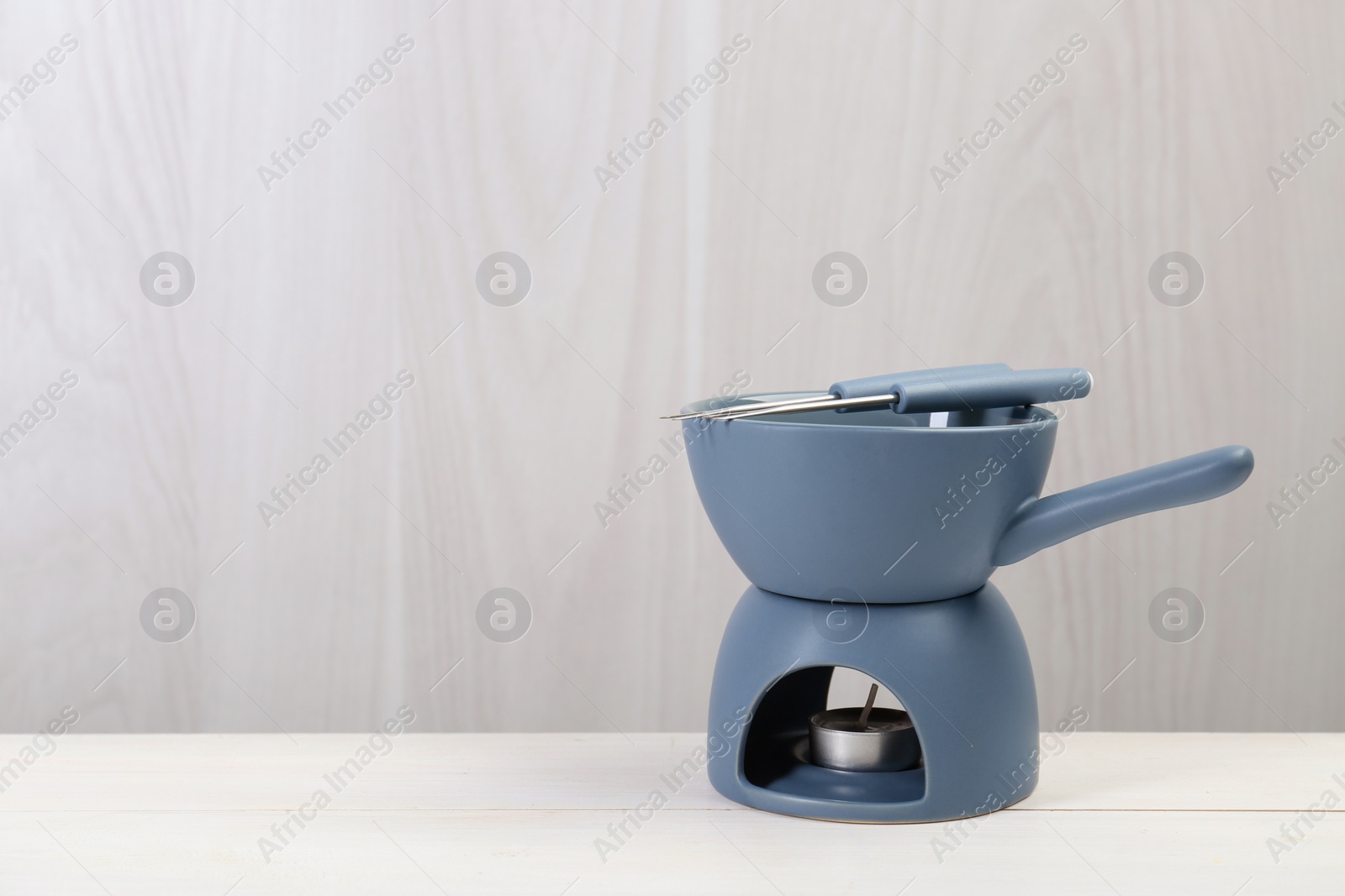 Photo of Fondue set on white wooden table, space for text