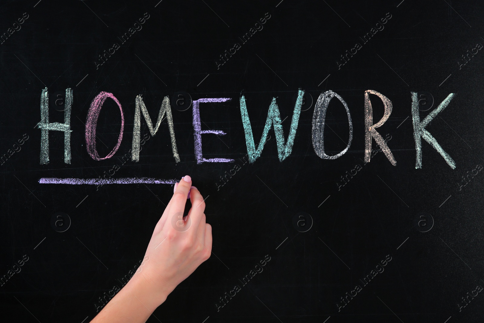 Photo of Woman writing word HOMEWORK on chalkboard, closeup