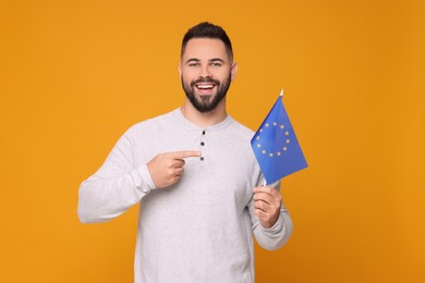Photo of Young man holding flag of European Union on orange background