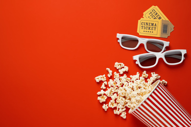 Photo of Overturned paper cup with delicious popcorn, cinema tickets and 3D glasses on red background, flat lay. Space for text