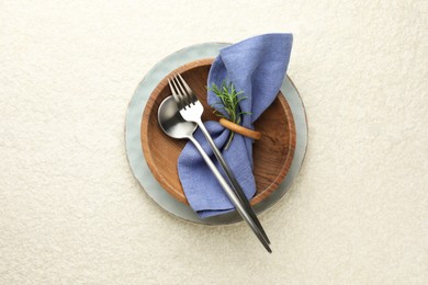 Stylish setting with cutlery, napkin, rosemary and plates on light textured table, top view. Space for text