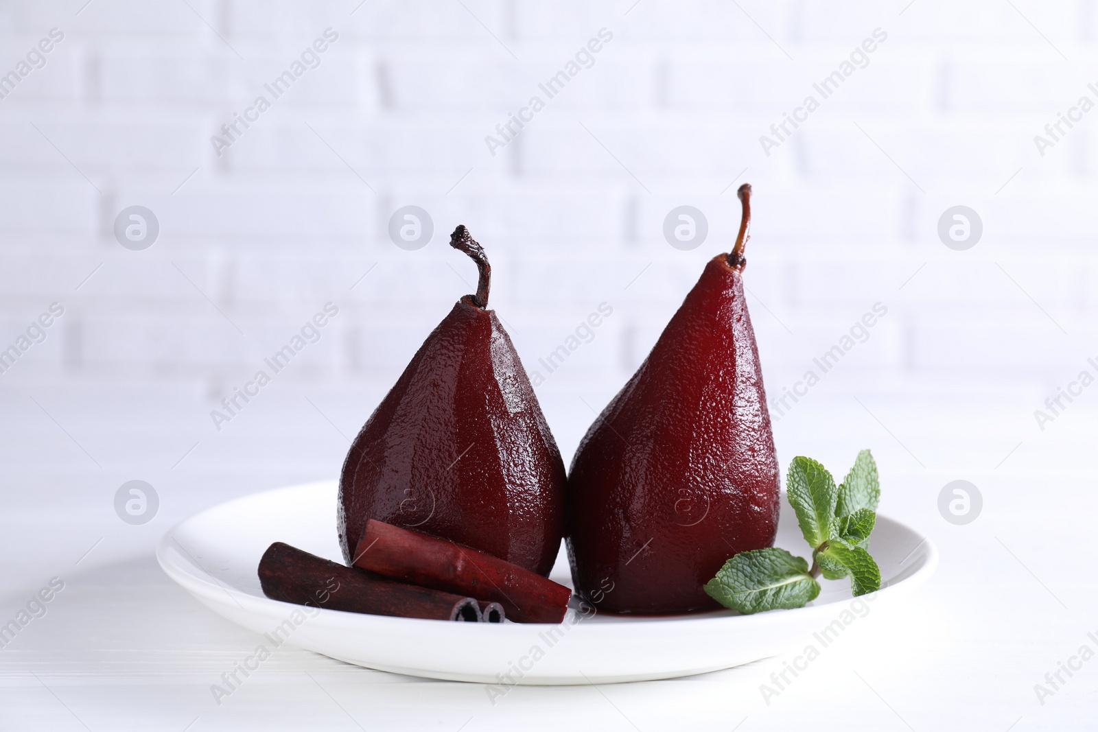 Photo of Tasty red wine poached pears with mint and cinnamon on white wooden table, closeup